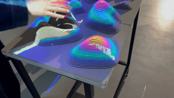 Hands interacting with the laser-cut, layered topographic contour models under colorful projected light