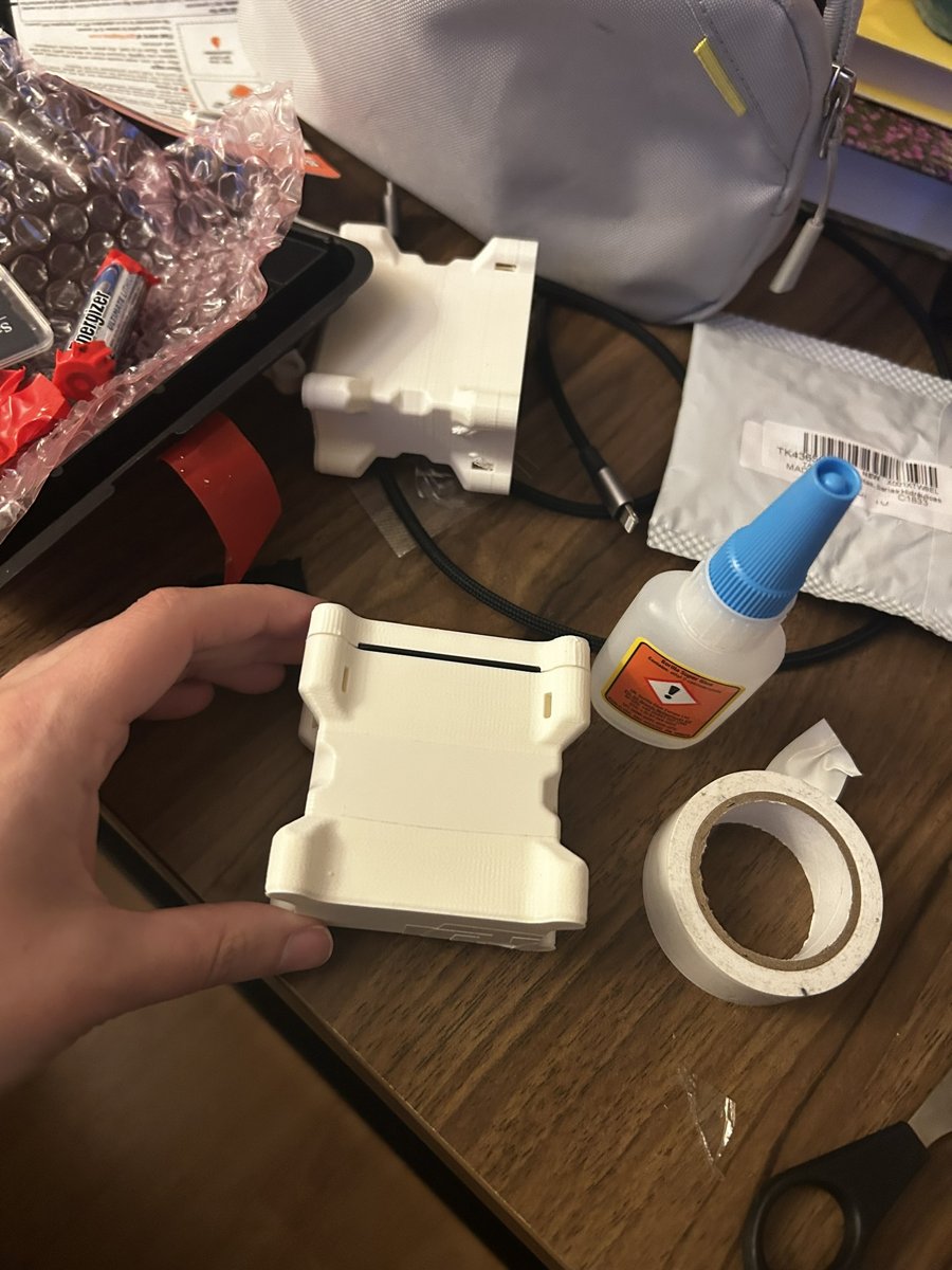 Hand-assembling a 3D-printed white hardware enclosure with glue and tape on a workbench